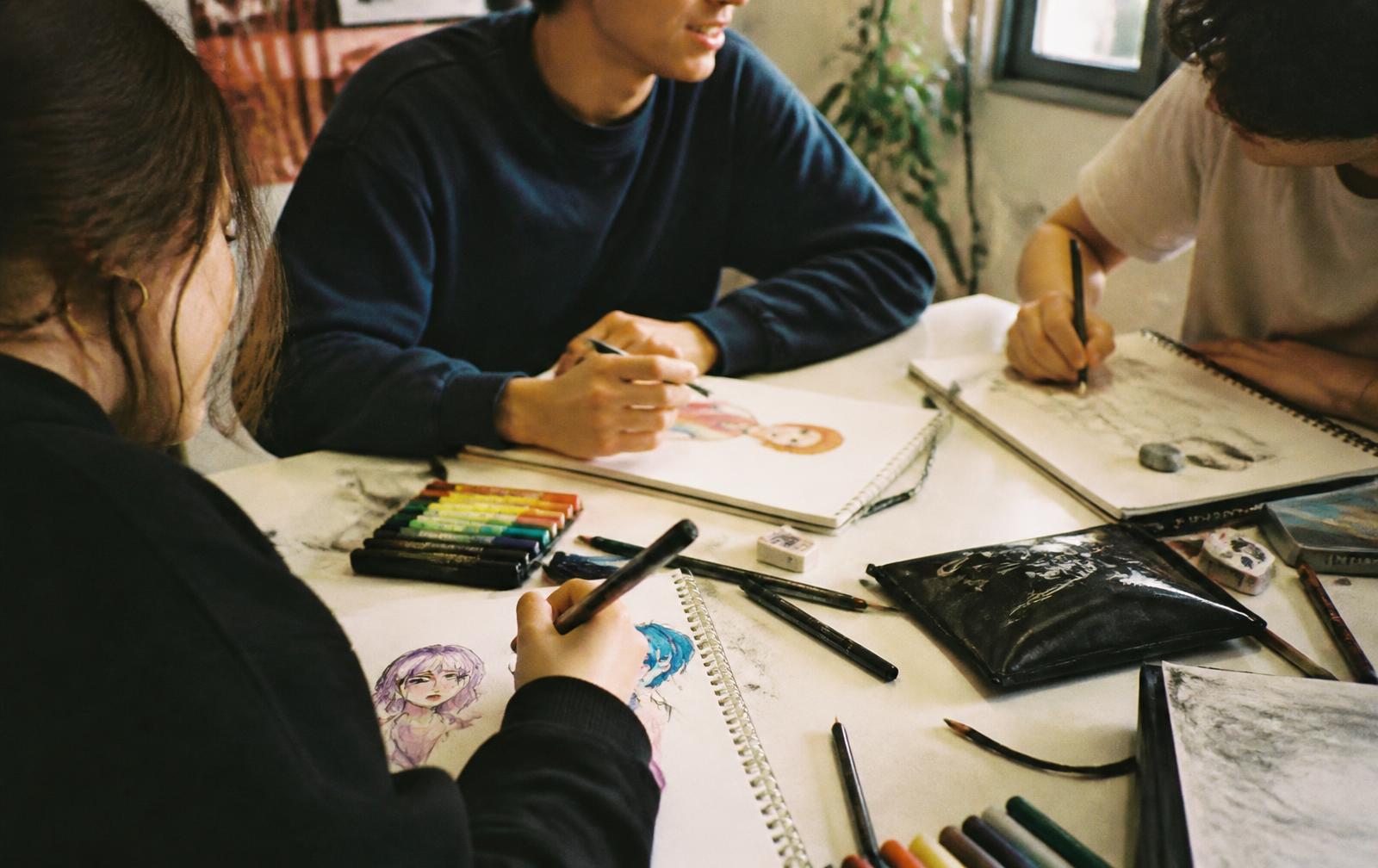 Teens drawing and painting together around a table during a workshop